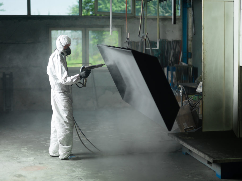Worker In Protective Gear Sandblasting a Metal Crate