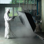 Worker In Protective Gear Sandblasting a Metal Crate