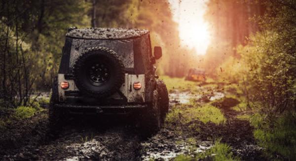 A Jeep drives through a muddy terrain